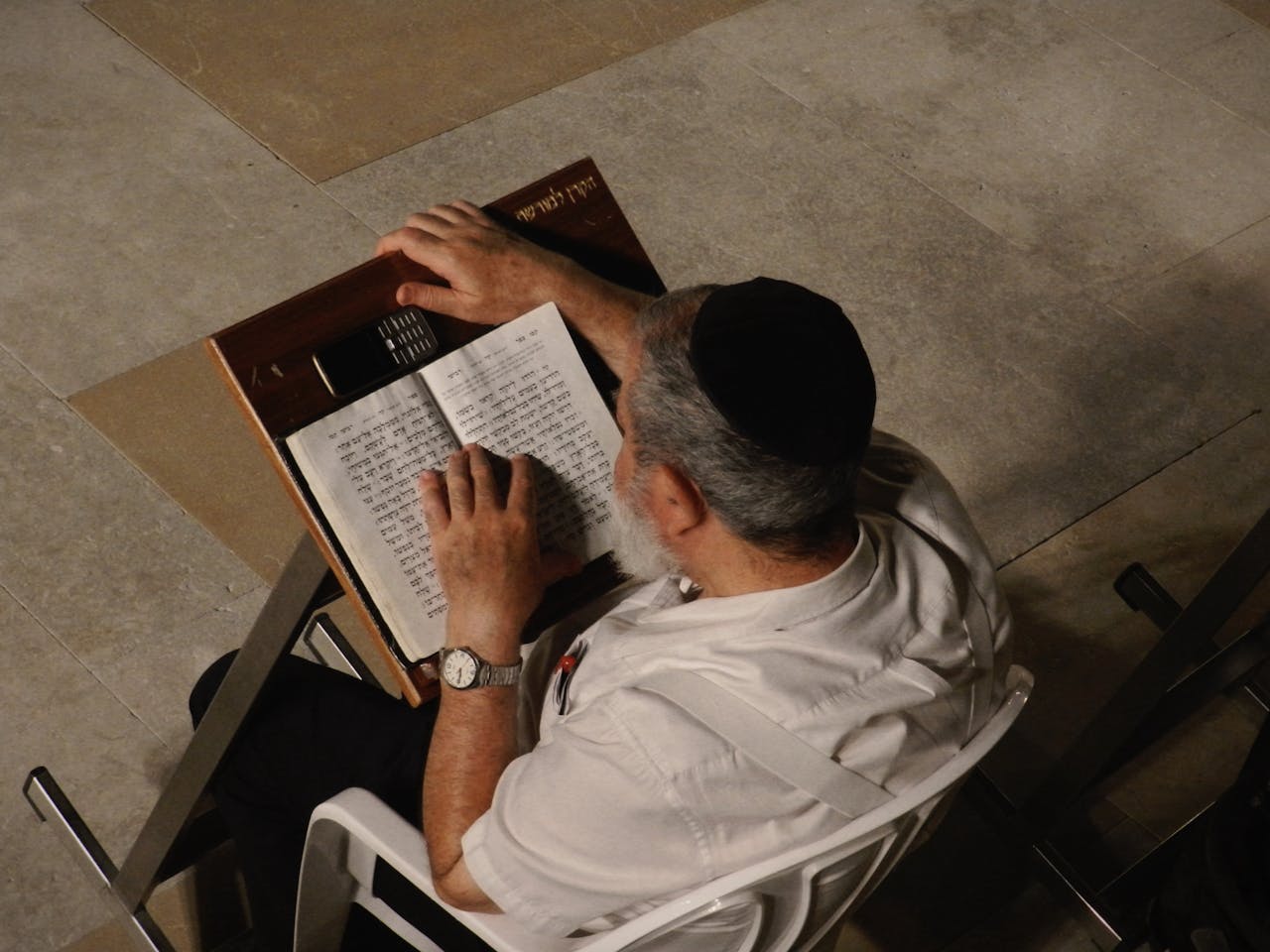 A man with a kippah reads a religious text in a peaceful setting, viewed from above.