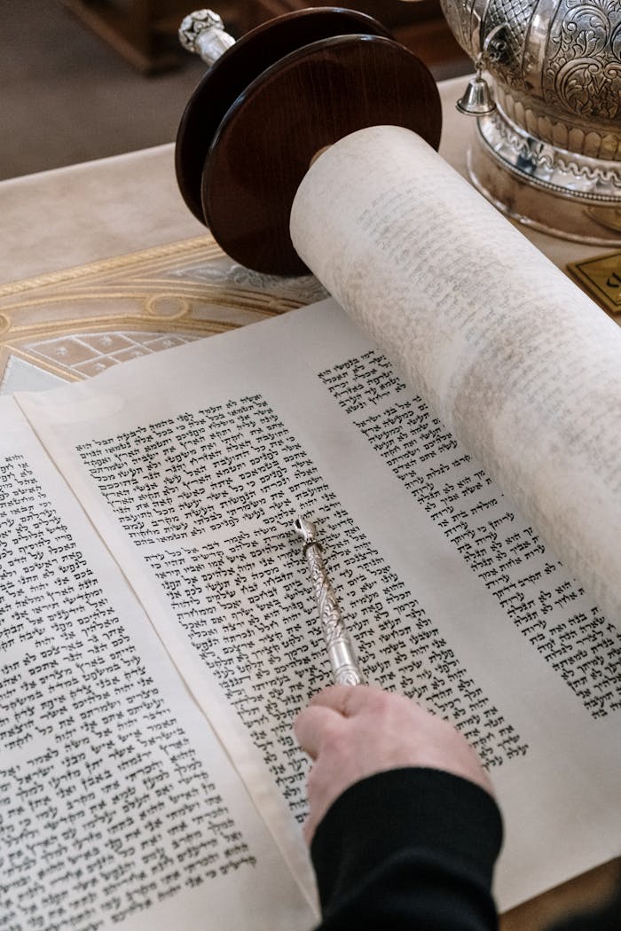 A detailed close-up of a Torah scroll with a yad pointer being used during a religious ceremony.